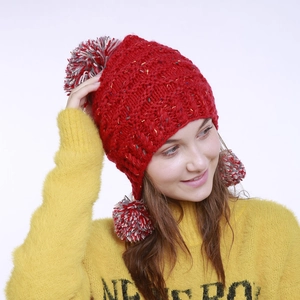 Detail der roten Strickmütze mit bunten Tupfen und drei flauschigen Bommeln am Modell