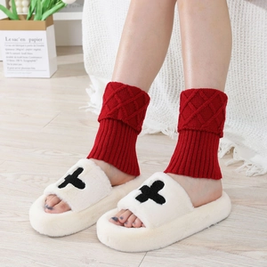 Close-up of red diamond knit leg warmers paired with white plush cross slippers