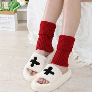 Detail of red cable knit leg warmers with diamond pattern and white plush slippers