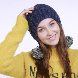 Detail der blauen Strickmütze mit Ohrenklappen und zwei grauen Bommeln am Model