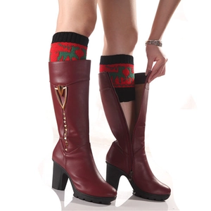 Jambières de Noël en tricot avec motifs rennes portées sur des bottes hautes rouges