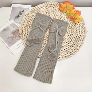 Kids grey knitted leg warmers with bows and pom-poms on a rustic autumn background