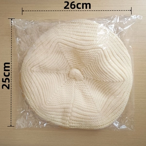 Flat lay of cream knitted beret showing size dimensions of 26cm by 25cm in clear packaging
