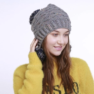 Graue Strickmütze mit Ohrenklappen und marineblauen Bommeln auf gelbem Pullover