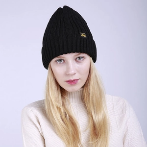 Detail of black cable knit beanie featuring a yellow label and thick winter texture