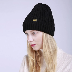 Detail of black cable knit beanie with yellow label patch and ribbed cuff texture