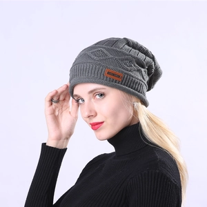 Detail of dark grey knit beanie featuring cable pattern and brown leather brand patch