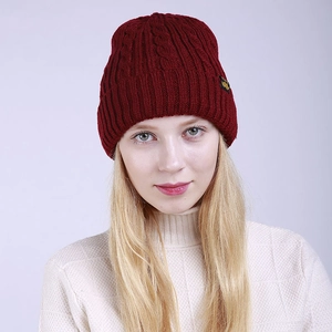 Close-up of dark red cable knit beanie featuring decorative side label and ribbed texture