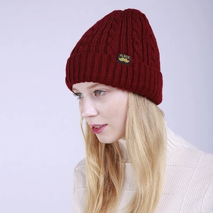Detail of wine red cable knit beanie with brand label and wide folded cuff on a model