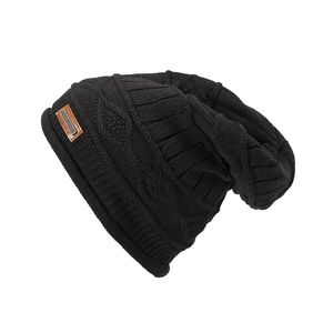 Detail of black cable-knit texture and brown leather logo patch on warm winter beanie