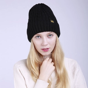 Detail of black cable knit beanie featuring thick ribbed texture and yellow side label
