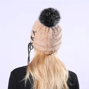 Detail der camel-farbenen Strickmütze mit großem Pelzpompon und XF SPORTS-Schriftzug