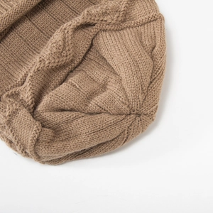 Macro view of the brown knitted hat's top closure showing detailed cable knit texture