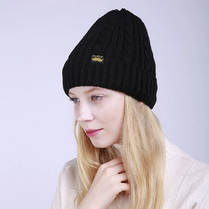 Detail of black cable knit beanie with brand label worn by model on grey background
