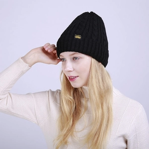Detail of black cable knit beanie with yellow circular Aluck patch and folded cuff edge