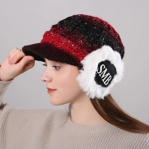 Detail of red and black checkered knit hat with white faux fur earflaps and SMB logo