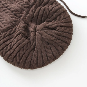 Detail of dark brown knit beanie with cable pattern and metal-capped drawstring top