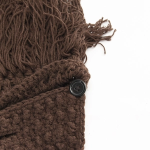 Macro shot of chunky dark brown knit texture with hanging tassels and a black button detail