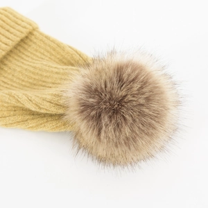 Detail van een mosterdgeel geribbelde gebreide muts met een pluizige bruine pompon