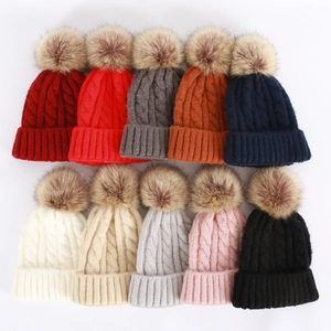 Close-up of thick cable knit beanies in various colors with fluffy faux fur pom-poms