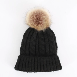Detail of chunky cable knit texture and large faux fur pom-pom on black winter hat