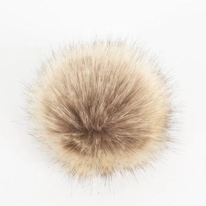 Detail van een donzige lichtbeige bontpompon met dicht haar voor winterse gebreide mutsen