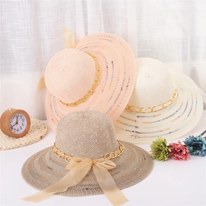 Détail de chapeaux de paille à larges bords avec chaîne dorée et nœuds en soie