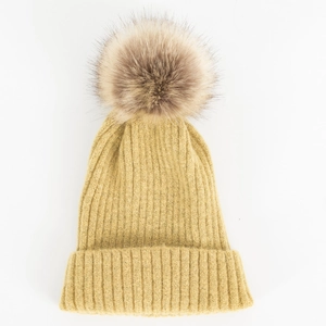 Detail van een gembergele geribbelde gebreide muts met een pluizige pompon van imitatiebont