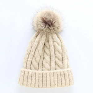 Thick cable knit beige beanie with a large brown faux fur pom pom for winter warmth