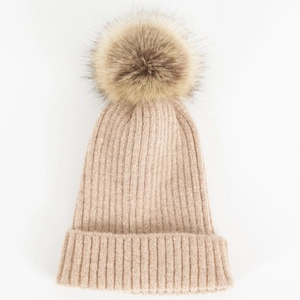 Detail van de beige gebreide muts met een grote bruine imitatiebont pompon op witte achtergrond