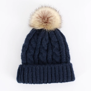 Close-up of thick cable knit texture on dark blue beanie with a large faux fur pompom