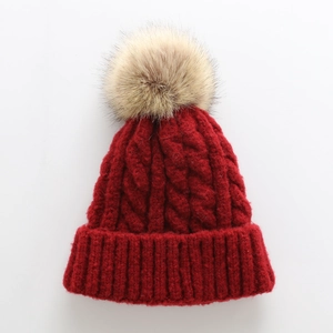 Detail of burgundy thick cable knit hat featuring a fluffy light brown faux fur pompom