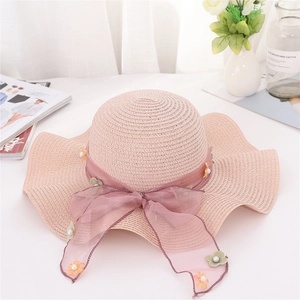 Dettaglio cappello di paglia rosa con tesa ondulata, fiocco in organza e decori di perle