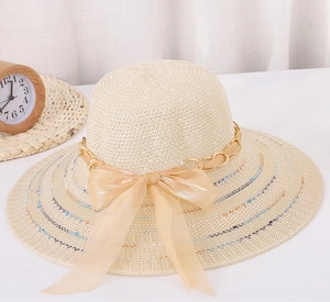 Détail d'un chapeau de paille beige à large bord avec chaîne dorée et nœud en mousseline