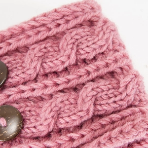 Macro shot of pink cable knit headband featuring textured patterns and brown buttons