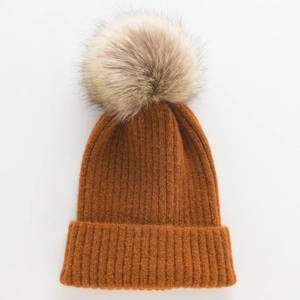 Detailopname van de karamelgekleurde gebreide muts met grote pompon van imitatiebont