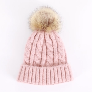 Close-up of pink knit beanie featuring chunky cable pattern and large faux fur pompom