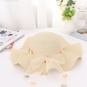 Dettaglio di un cappello di paglia beige con fiocco in tulle, perle e delicati fiori decorativi