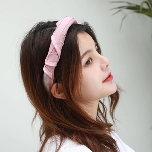 Side view of woman wearing a pink pleated fabric headband with twisted design detail