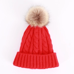 Detailed close-up of chunky cable knit texture and faux fur pompom on red winter beanie