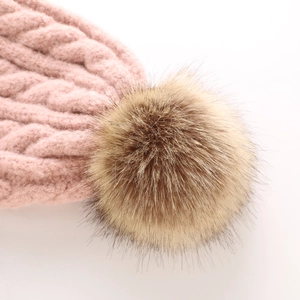 Close-up of pink cable knit hat featuring a large fluffy faux fur pompom detail