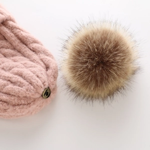 Close-up of pink cable knit hat with a detachable faux fur pompom and bronze snap