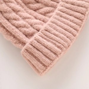 Detail of pink knitted beanie featuring chunky cable knit patterns and ribbed cuffs