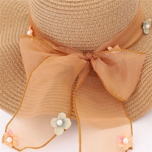 Dettaglio del cappello di paglia con fiocco in organza, fiori a rilievo e perle bianche