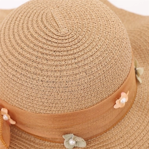 Dettaglio cappello di paglia con nastro di raso, fiori in tessuto e perle decorative