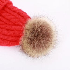 Detail of red cable-knit beanie featuring a fluffy light brown faux fur pom-pom