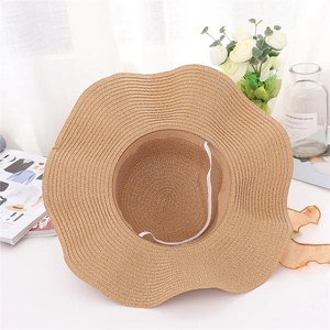 Dettaglio cappello di paglia a tesa ondulata, trama naturale e cinturino elastico bianco