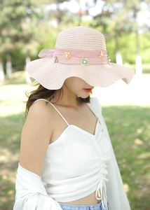 Dettaglio cappello di paglia rosa a tesa larga con nastro in chiffon e decorazioni floreali