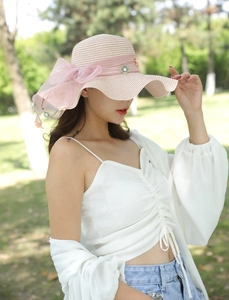 Dettaglio cappello di paglia rosa con grande fiocco in tulle e decorazioni floreali di perle