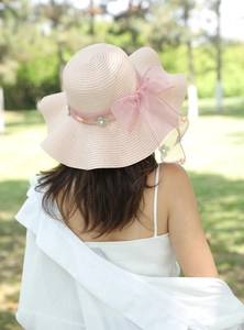 Dettaglio di cappello di paglia rosa a tesa larga con fiocco in chiffon e fiori